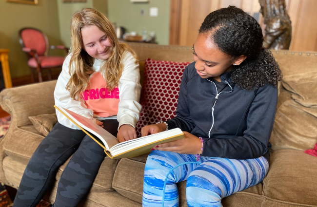 2 Woodward students looking at a book while seated on a couch