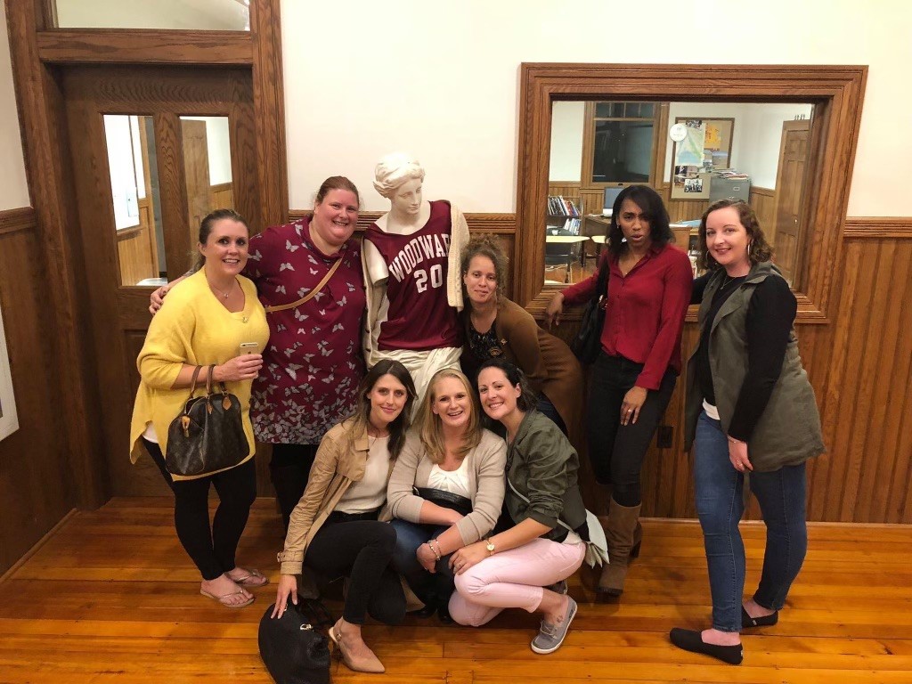 Woodward alumnae pose inside with mannequin dressed in Woodward Athletic gear